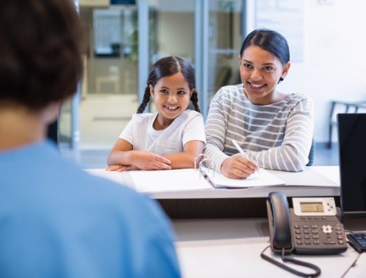 Mother and daughter smiling at dental office reception desk