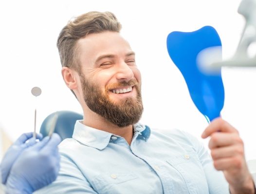 Man in dental chair looking at smile in mirror