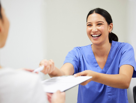 a dental assistant handing a patient a pen and paperwork