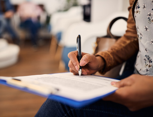 a woman filling out patient forms on a blue clipboard