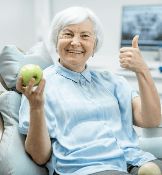 Woman in dental chair giving a thumbs up and holding a green apple