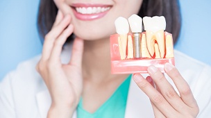 Smiling woman holding up a dental implant replacement tooth model