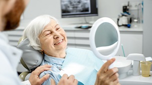 Woman looking at smile in the mirror after dental implant tooth replacement