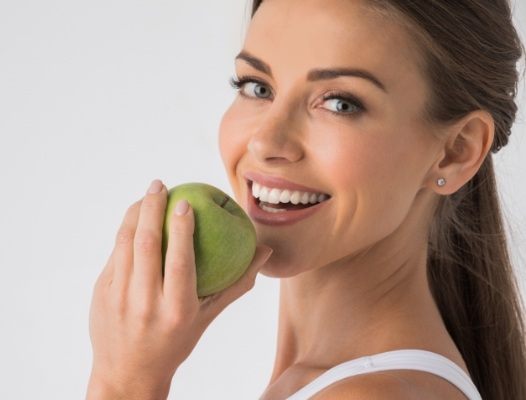Woman eating a green apple after dental implant tooth replacement