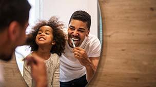 Father and daughter brushing to prevent dental emergencies in DuPont