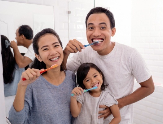 Family of three brushing teeth together