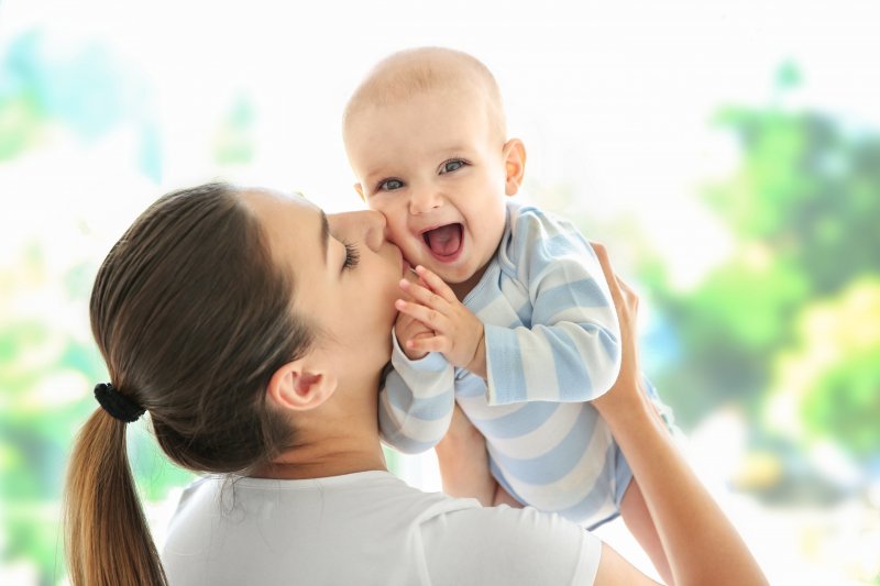 a woman holding up her baby and kissing it on the cheek