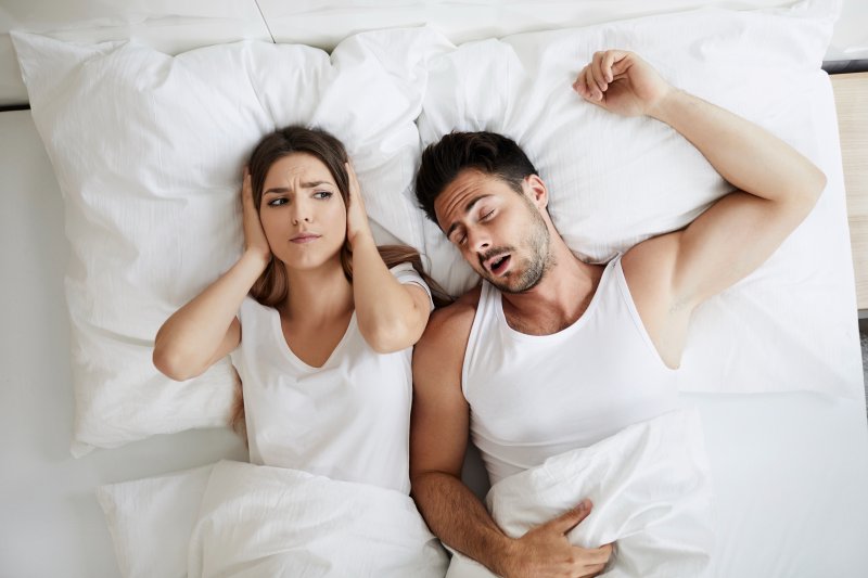 a man asleep with a woman putting her hands over her ears