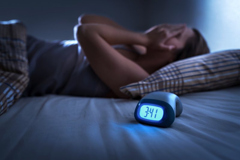 a woman lying in bed with her hands over her face and an alarm clock reading 3:41 a.m. 