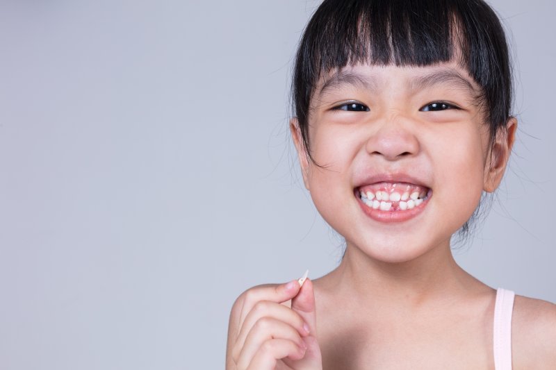 a little girl smiling wide while holding a tooth she recently lost