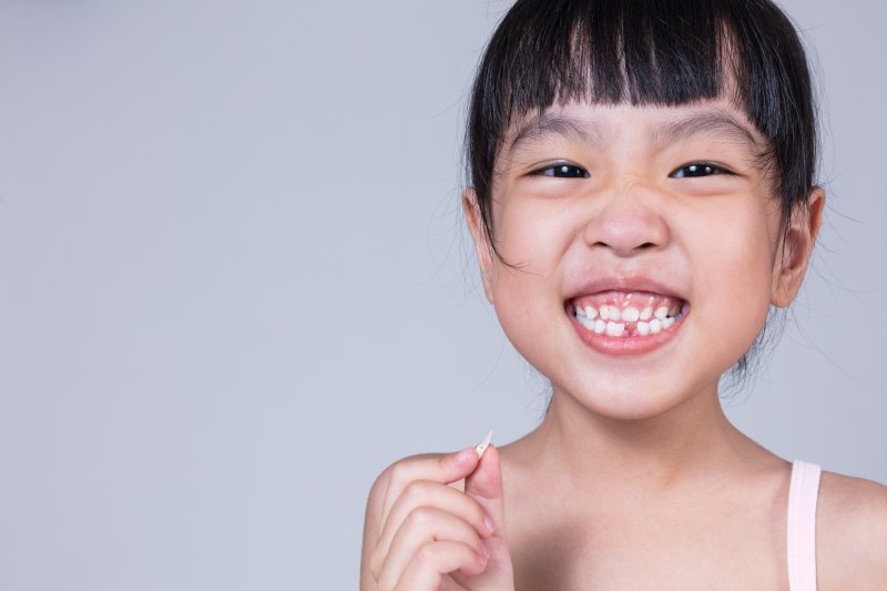 a little girl smiling wide while holding a tooth she recently lost 