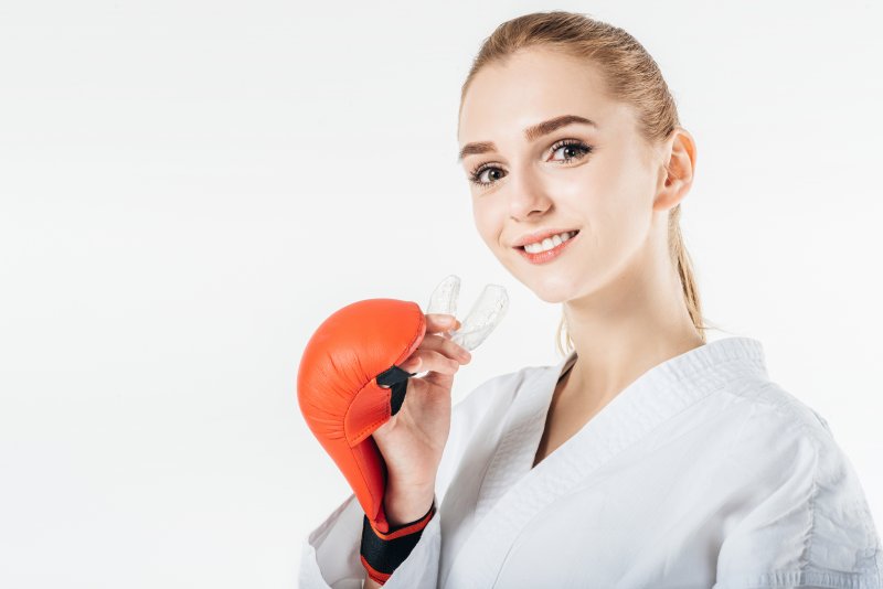 a young girl wears a karate robe and boxing glove while preparing to insert a mouthguard