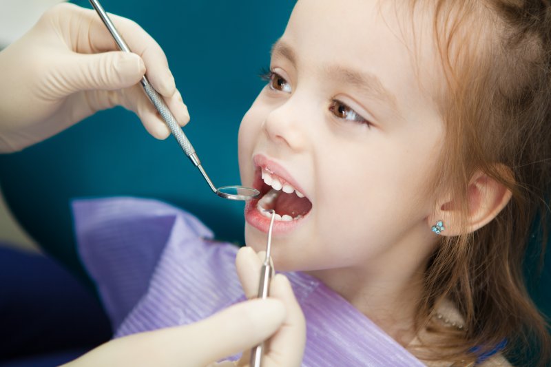 a little girl having her teeth checked by her dentist during a regular exam