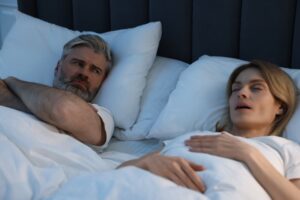 a woman snoring and her husband looking at her annoyed