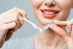a woman putting whitening gel in a dental tray