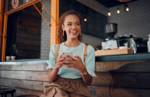 a smiling woman holding her phone and sitting at a bar in a coffee shop