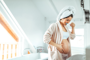pregnant woman brushing her teeth and touching her belly